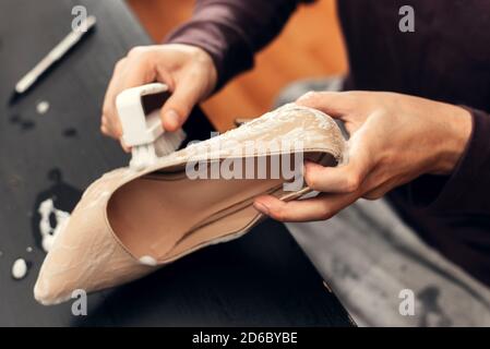 Ein Mann putzt Damenschuhe mit einer Bürste. Reinigen des Schuhs von Schmutz. Stockfoto