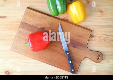 Draufsicht auf Red Bell Pepper auf einem Schneidbrett Mit Messer und zwei Paprika auf Holztisch Stockfoto