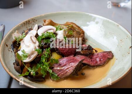 Eine Mahlzeit mit Fleischsteak mit Pilzen und Tomaten Serviert in einem grauen rustikalen Teller in Restaurant-Umgebung Stockfoto