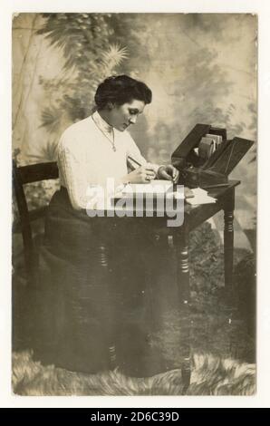 Anfang 1900 post Edwardian Ära Studio Portrait Postkarte von attraktiven Frau, genannt Trixie B. Neville, sitzt an einem Schreibtisch, datiert Weihnachten 1912 auf der Rückseite, Großbritannien Stockfoto