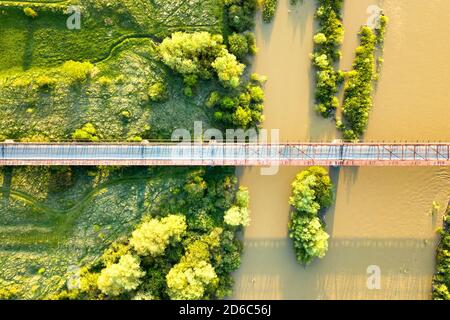 Luftaufnahme einer schmalen Straßenbrücke, die sich über einen schlammigen, breiten Fluss in grüner ländlicher Umgebung erstreckt. Stockfoto