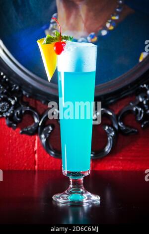 Blue Drink Cocktail mit Schaum verziert Ananas und Kirsche in großen Glas auf dem Hintergrund des Bildes im Rahmen. Stockfoto