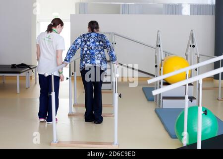 Physiotherapeut hilft dem Patienten, zwischen den parallelen Balken zu gehen. Stockfoto