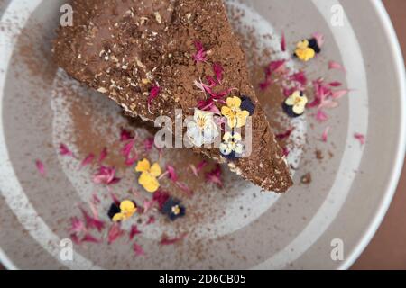 Draufsicht auf ein Stück Schokoladenkuchen mit essbaren Blumen. Weiche Ansicht Stockfoto