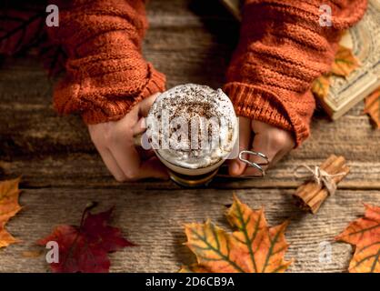 Hand hält warmen Kürbis Gewürz Latte oder Kaffee. Flache Laie im Herbststil. Gemütliches warmes Bild eines Mädchens Hände mit einer Tasse leckeren Drink. Stockfoto