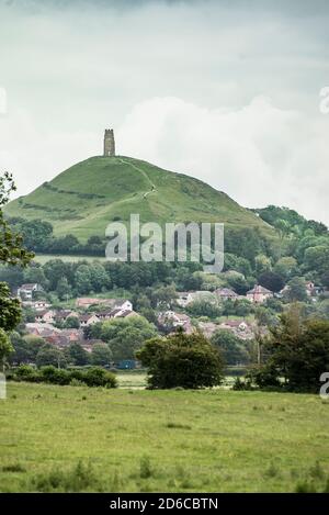 Das geheimnisvolle Glastonbury Tor regiert die New Age Stadt Glastonbury, England. Sommer Grün und Ackerland im Vordergrund gibt eine idyllische Atmosphäre. Stockfoto