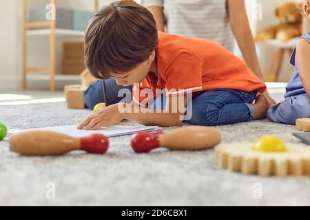 Vorschulkinder zeichnen ein Bild mit Bleistiften sitzen auf warmen Teppich Mit seinem Bruder und Kindermädchen Stockfoto