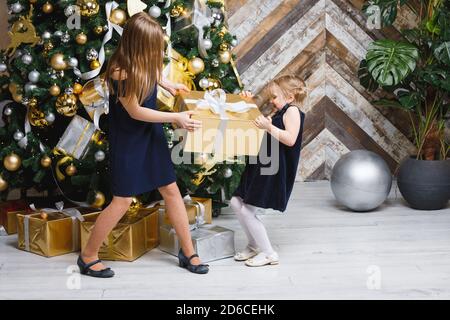 Zwei Schwestern tragen blaue Kleider ziehen große golden verpackt Geschenk Box in der Nähe von geschmückten Weihnachtsbaum kann kein Geschenk auf teilen Boxtag Stockfoto