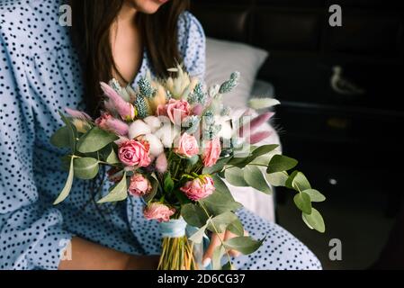 Mädchen mit einem Blumenstrauß aus der Nähe. Frau sitzt auf einem Bett in einem blauen Kleid und hält getrocknete Blumen. Konzept der Hochzeit, Beziehungen und Stockfoto