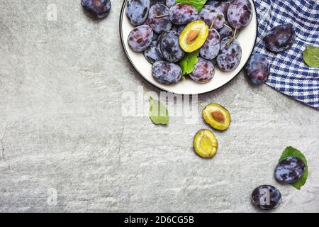 Viel frische süße Pflaumen auf einem Teller mit Blättern, Draufsicht mit Platz für Text. Gesunde Früchte. Stockfoto