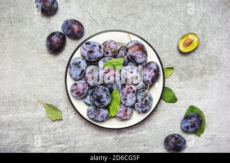 Viel frische süße Pflaumen auf einem Teller mit Blättern, Draufsicht mit Platz für Text. Gesunde Früchte. Stockfoto