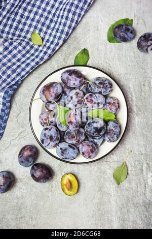 Viel frische süße Pflaumen auf einem Teller mit Blättern, Draufsicht mit Platz für Text. Gesunde Früchte. Stockfoto