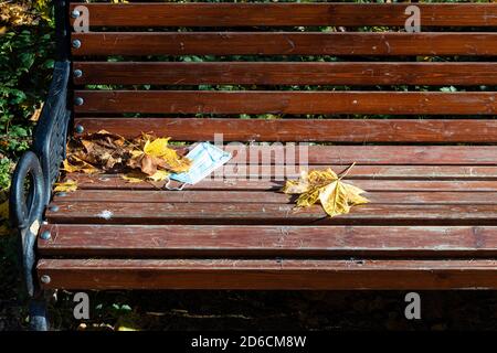 Verlassene medizinische Gesicht fask und gefallen Ahornblätter auf Holz Bank im Stadtpark am Herbsttag Stockfoto