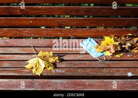 Verlassene medizinische Gesicht fask und gefallen Ahornblätter an der Oberfläche Von Holzbank Nahaufnahme am Herbsttag Stockfoto