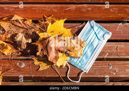 Draufsicht auf Falled Medical Face fask und gefallen Ahorn Blätter auf Holzbank schließen am suny Herbsttag Stockfoto