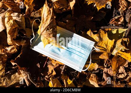 Fallengelassene Sanitär-Gesichtsmaske in gefallenen Blättern aus nächster Nähe Sonniger Herbsttag Stockfoto