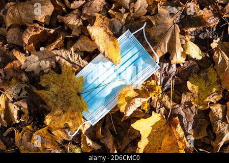 Geworfen Sanitär Gesichtsmaske in Ahornblätter Nahaufnahme auf Sonniger Herbsttag Stockfoto
