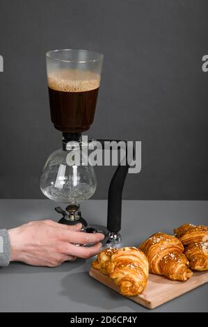 Menschliche Hand stellt die Kaffeekanne für die Zubereitung von Tropfkaffee in einem Raum mit grauen Wänden ein. Stockfoto