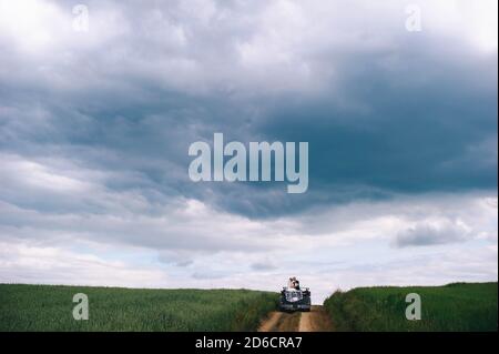 Jungvermählte reiten in einem Cabrio auf einem Feld mit Mohnblumen vor einem Gewitter. Stockfoto