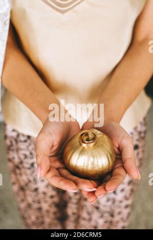 Frauen Hände halten einen kleinen Kürbis in Gold mit Eheringe auf sie gemalt. Stockfoto