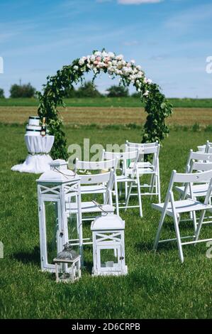 Runder Hochzeitbogen mit Pfingstrosen und Grün mit Weiß dekoriert Sessel für Gäste im Freien Stockfoto