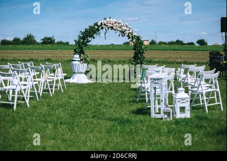 Runder Hochzeitbogen mit Pfingstrosen und Grün mit Weiß dekoriert Sessel für Gäste im Freien Stockfoto