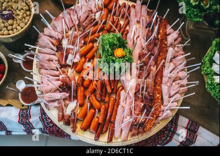 Draufsicht auf einen runden Holzteller mit verschiedenen Fleischsorten und Würstchen auf Spieße. Stockfoto