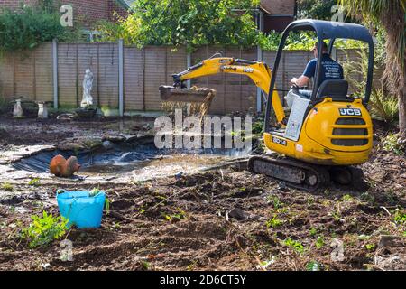 Gartenabräumarbeiten und Renovierungen, die im Oktober im Garten in Bournemouth, Dorset UK, stattfinden - Rodung des Gartenteiches mit jcb-Minibagger Stockfoto