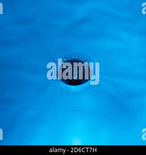 Wassertropfen, der in Wasser fällt und einen perfekten Tropfen spritzt In blau Stockfoto