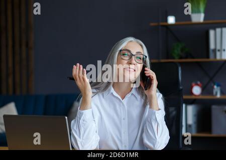Lächelnd ältere grauhaarige schöne Geschäftsfrau, die im Büro telefoniert. Geschäftsporträt der attraktiven reifen Dame trägt Brillen Stockfoto