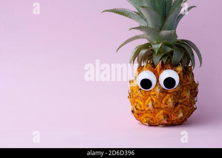 Lustige exotische Ananas mit schönen Augen auf rosa Hintergrund Stockfoto