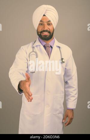 Junge gutaussehende indische Sikh Mann Arzt vor grauem Hintergrund Stockfoto