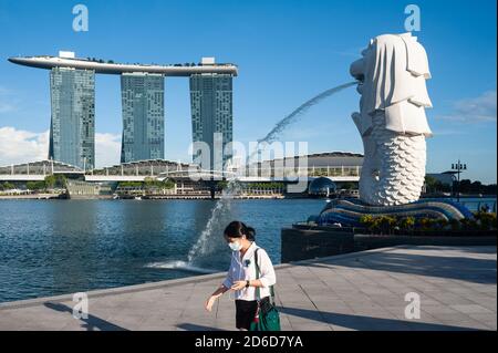 23.09.2020, Singapore, , Singapur - EINE Frau mit Gesichtsmaske läuft durch den Merlion Park mit der Fountain Statue am Ufer des Singapore R Stockfoto