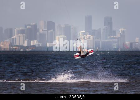 Ein Kitesurfer springt vom Wasser mit der Miami Skyline in der Ferne. Stockfoto