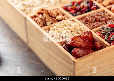 Zutaten für die Herstellung von Müsli. Getrocknete Früchte, verschiedene Nüsse und Samen in einer Holzkiste. Selektiver Fokus. Stockfoto