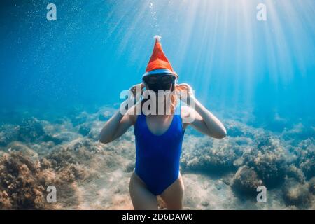 Glückliche Freitaucherin Frau mit Weihnachtsmütze posiert unter Wasser im blauen Ozean. Weihnachtsferien Konzept Stockfoto