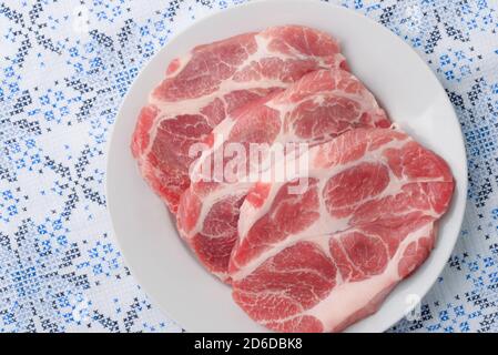 Draufsicht auf drei rohe, frische Schweinehals-Fleischsteaks Auf weißem Teller Stockfoto