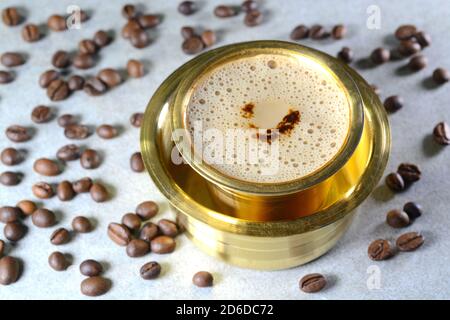 Indischer Filter Kaffee serviert in Messingbecher mit Kaffeebohnen Stockfoto