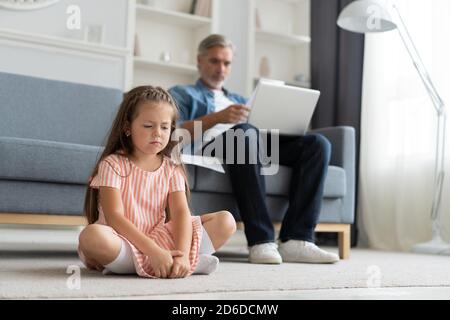 Keine Zeit Für Kind. Grauhaarige Papa beschäftigt mit Laptop, online zu Hause arbeiten, traurig gelangweilt beleidigt Tochter sitzt in der Nähe Stockfoto