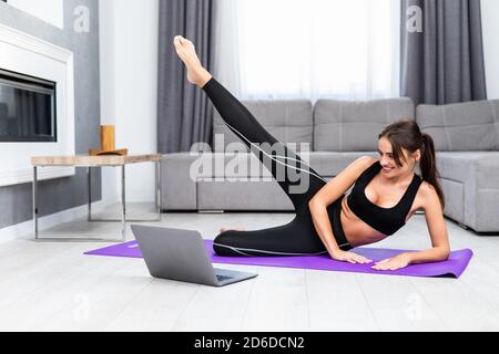 Schöne junge Frau tut Plank Übung im Wohnzimmer zu Hause, Videos auf Laptop-Computer und Online-Anweisungen wiederholen, kopieren Raum. F Stockfoto