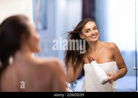 Junge hübsche Frau, die nach der Dusche mit dem Fön im Badezimmer einen Bademantel trug Stockfoto