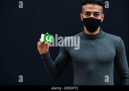 Mittelöstlicher Mann in grauem Rollkragen und schwarzer Gesichtsschutzmaske zeigen Pakistan Flagge isolierten Hintergrund. Stockfoto