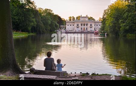 Eine Frau und ein kleines Mädchen sitzen am Teich mit Blick auf den Palast in Lazienki Stockfoto