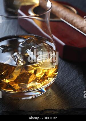 Whisky auf den Felsen und eine Zigarre in einem Aschenbecher Auf einer schwarzen Schieferfläche Stockfoto