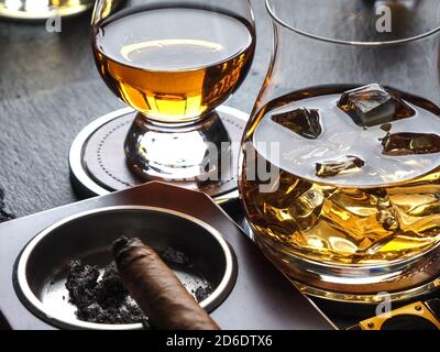 Whisky auf den Felsen und eine Zigarre in einem Aschenbecher Auf einer schwarzen Schieferfläche Stockfoto