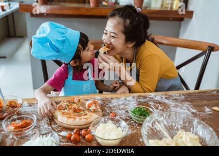 Junge Mutter und ihre kleine Tochter essen Pizza und mit Spaß Stockfoto