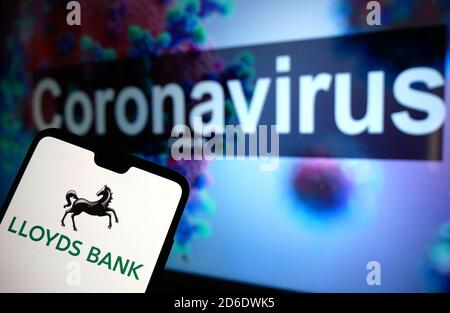 Das Lloyds Bank-Logo auf einem Mobiltelefon mit einem illustrativen Modell des Coronavirus auf einem Monitor im Hintergrund. Stockfoto