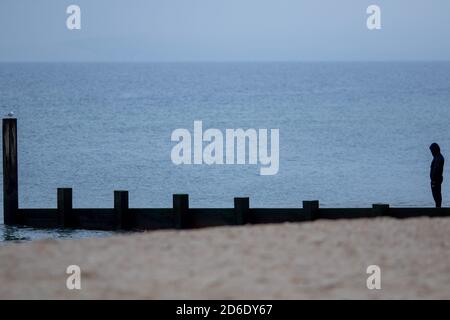 Ein Mann steht mit seiner Haube silhouetted gegen das Wintermeer und Himmel neben einem der vielen Groynes oder Wellenbrecher am Strand bei Fisherman’s Walk in Bournemouth. 29. Januar 2015. Foto: Neil Turner Stockfoto