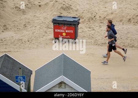 Zwei Männer joggen entlang der Promenade neben dem Strand, während der Sand am Fisherman’s Walk in Bournemouth auftürmt. 23. Oktober 2019. Foto: Neil Turner Stockfoto