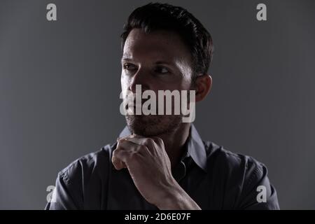 Junger Mann mit der Hand auf dem Kinn vor grauem Hintergrund Stockfoto